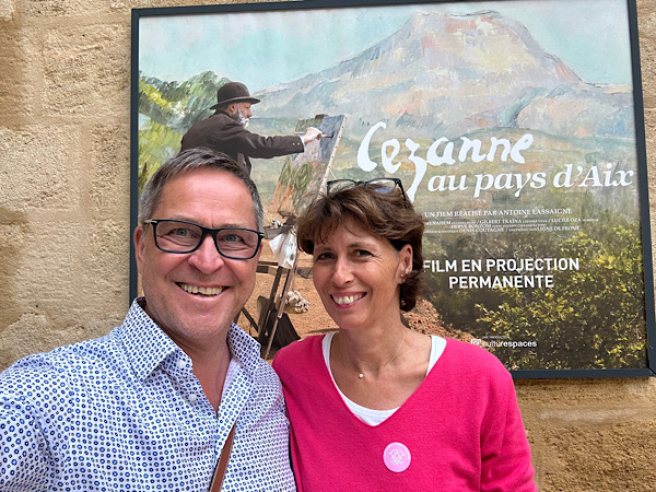 Frau und Mann stehen vor einer Wand mit einem Plakat, das auf den Maler Cezanne und sein Wirken in der Provence hinweist