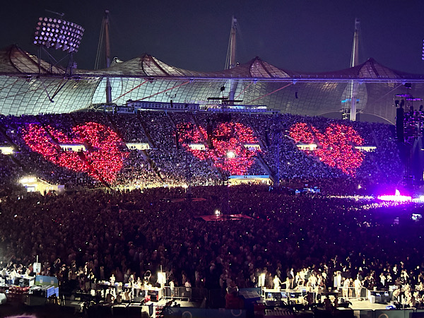 Münchener Olympiastadion, Dämmerung, drei rote Herzen leuchten auf den Zuschauerrängen auf