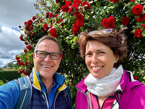 Frau und Mann stehen vor einem großen Busch mit bkühenden roten Rosen