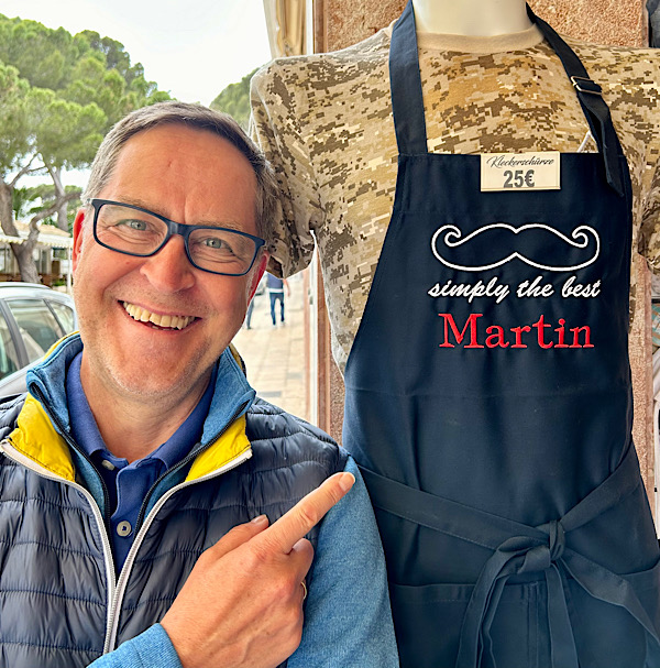 Mann mit Brille (Martin) steht neben einer Puppe und zeigt auf deren Kochschürze, auf der steht: "Martin - simply the best"