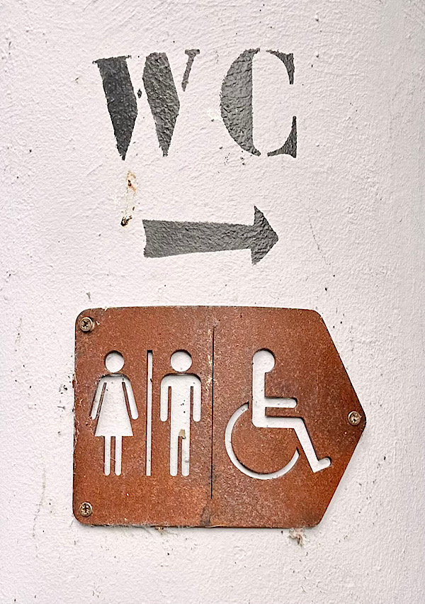 Schriftzug WC an einer Mauer sowie das Zeichen für normale und Behindertentoiletten