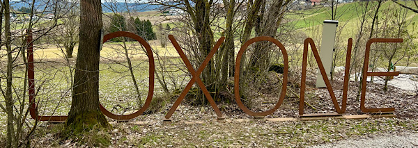 Landschaft, Wiesen Bäume und im Vordergrund in rostenden Stahl-Lettern der Schriftzug "LOXONE"