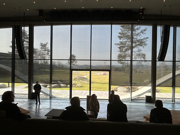 Großer Saal mit riesigen Fenstern, die den Blick in die Umgebung freigeben. Die Schatten von Menschen im Vordergrund