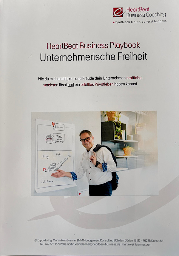 Cover eines Din-A4 Arbeitsbuches mit dem Titel: HeartBeat Business Playbook - Unternehmerische Freiheit. Darunter ein Bild von Mann mit Brille (Martin) leger im weißen Hemd mit Sakko über der Schulter, zeigt auf ein Flipchart mit Illustrationen